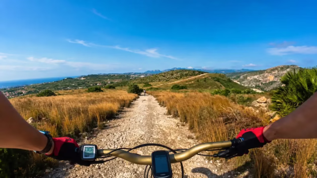 Mountain biking on a rocky trail above Jávea with Mediterranean Sea and coastal mountains in the background.